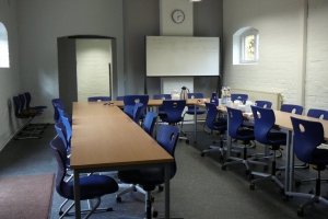 Ein Besprechungsraum mit Tischen und blauen Stühlen sowie einem Whiteboard, auf dem einige Notizen stehen