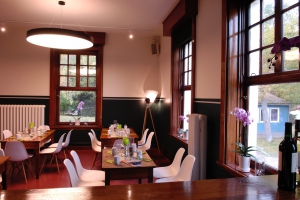 Das Restaurant in kompletter Ansicht mit dunklen Tischen, weißen Stühlen und grün-weißer Tischdekoration